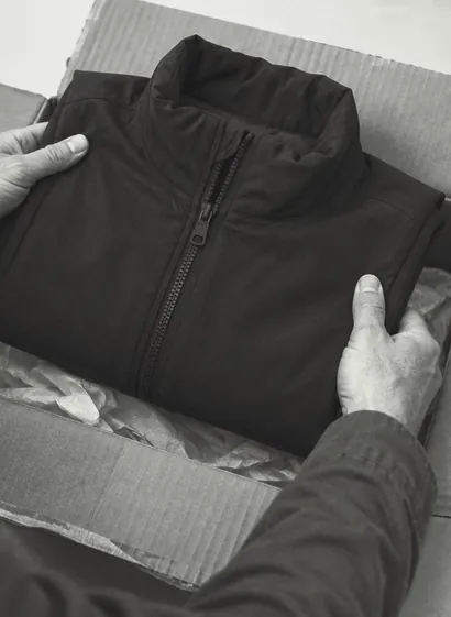 Hände heben eine Jacke aus einem geöffneten Rücksendepaket
